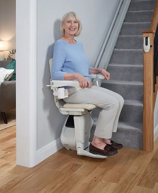 An elderly woman uses her newly installed straight Handicare 1100 which is at the bottom of the stairs.