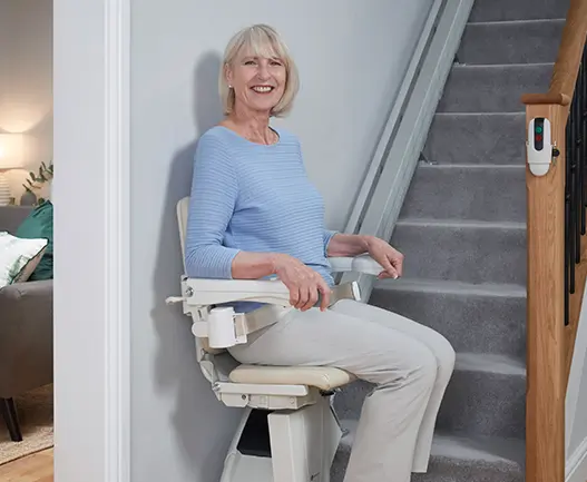 An elderly woman uses her newly installed straight Handicare 1100 which is at the bottom of the stairs.