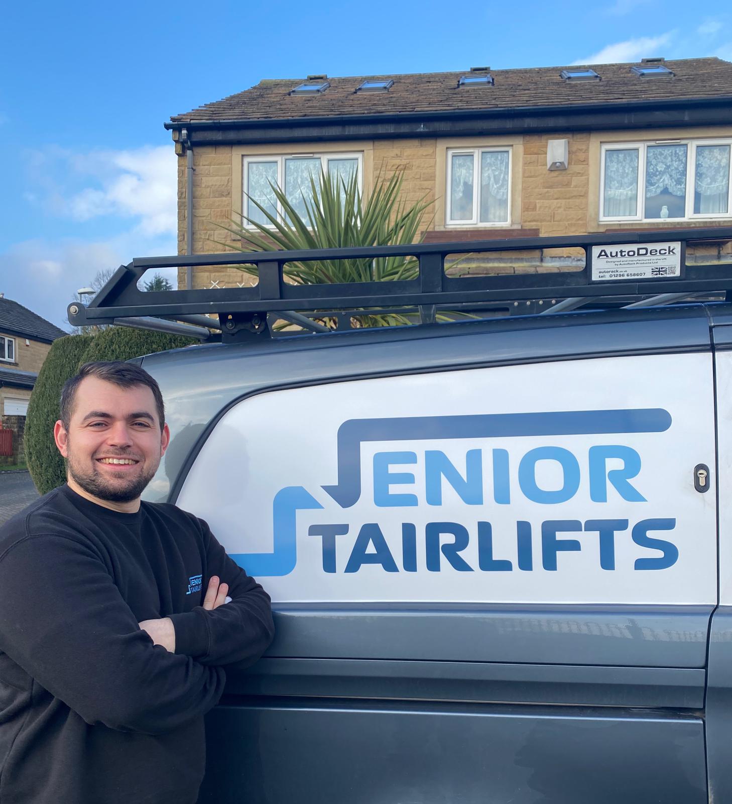 An engineer smiles beside a branded 'Senior Stairlifts' van.