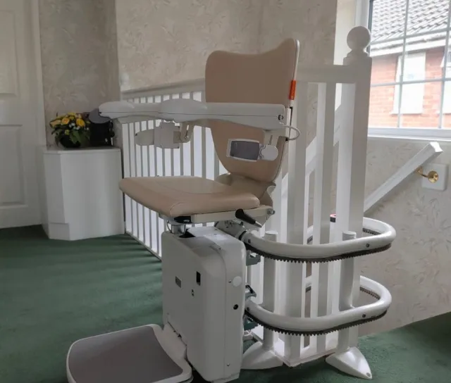 A curved stairlift waits at the top of a set of stairs.