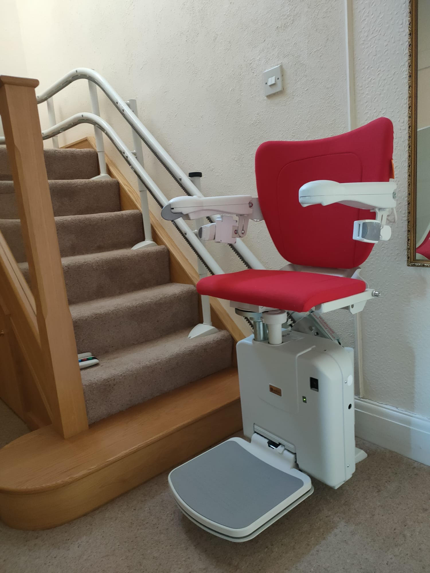 Reconditioned Stairlift with red upholstery and folded out foot rest.