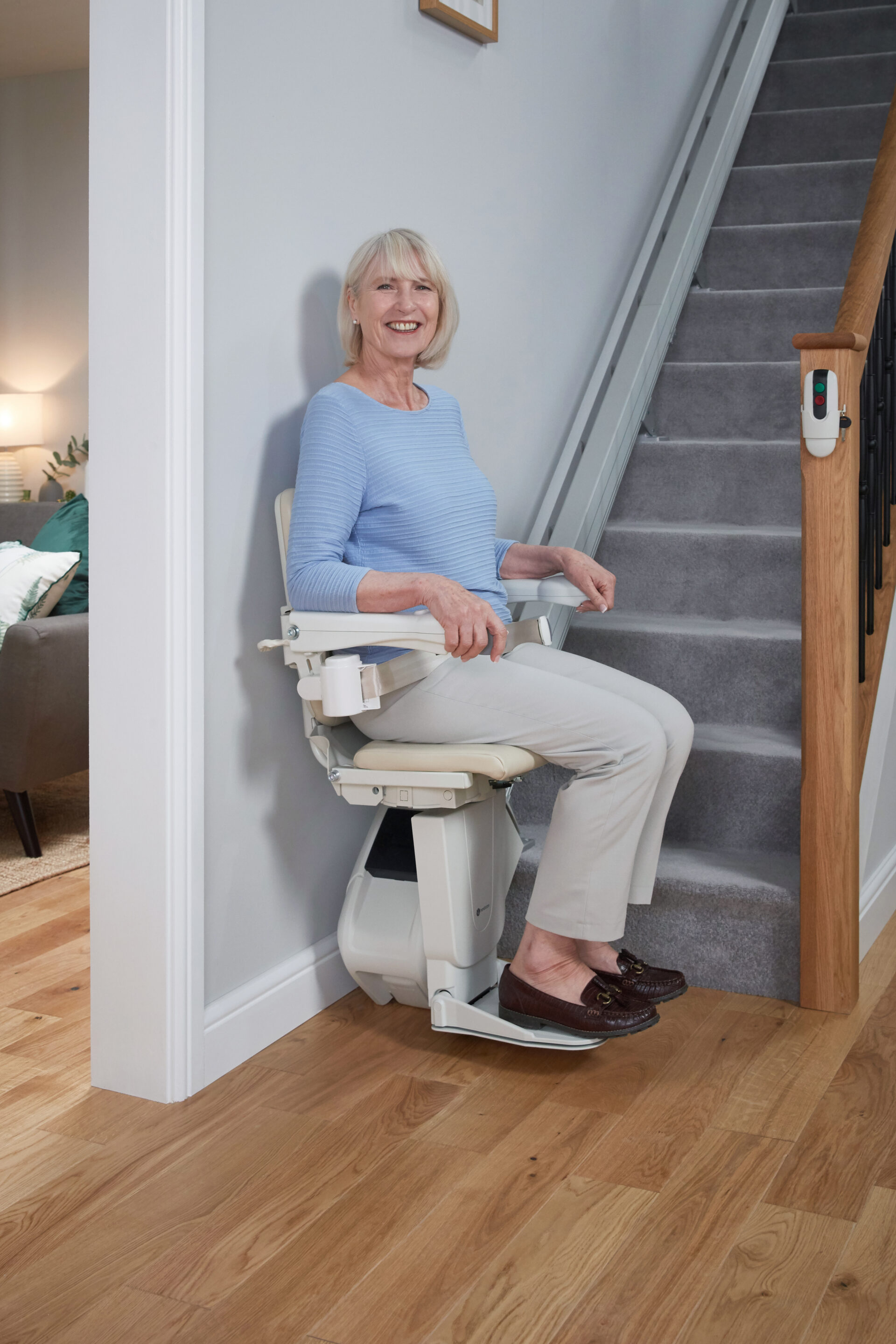 An elderly woman smiles whilst using a Handicare 1100 straight stairlift.