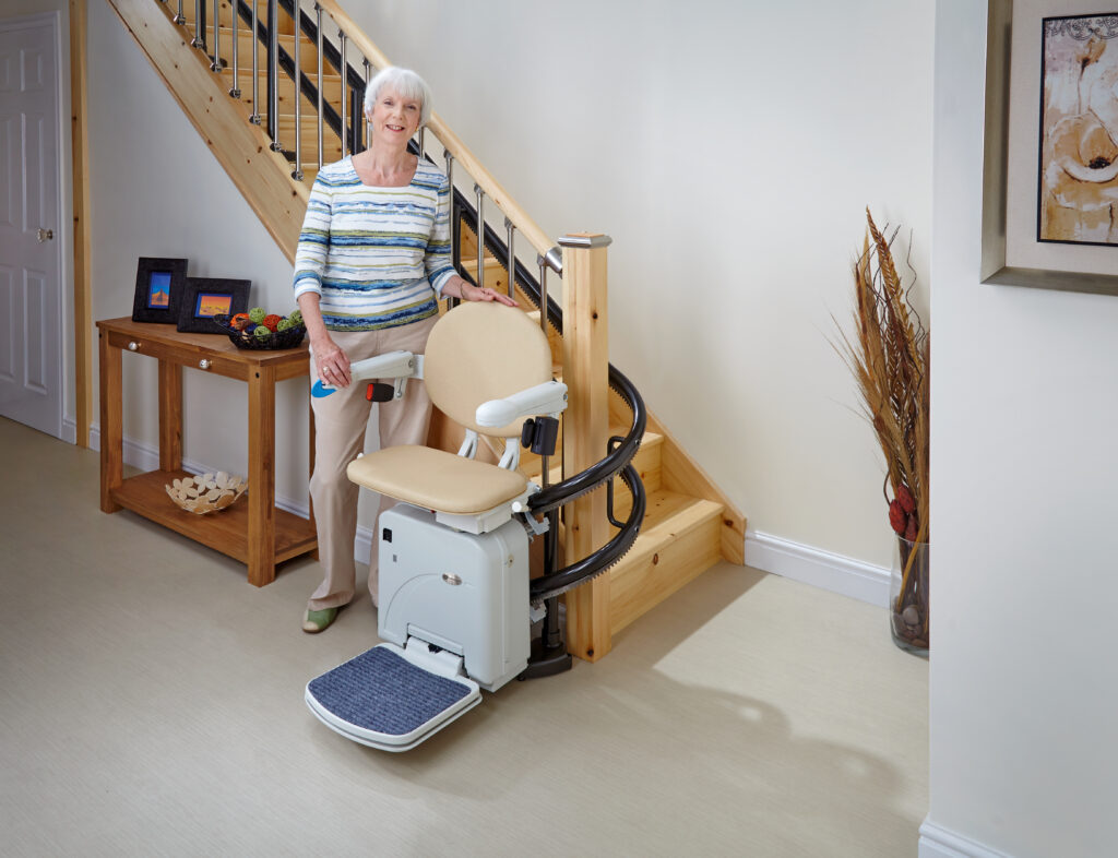 An elderly woman happily stands by her Curved Stairlift.