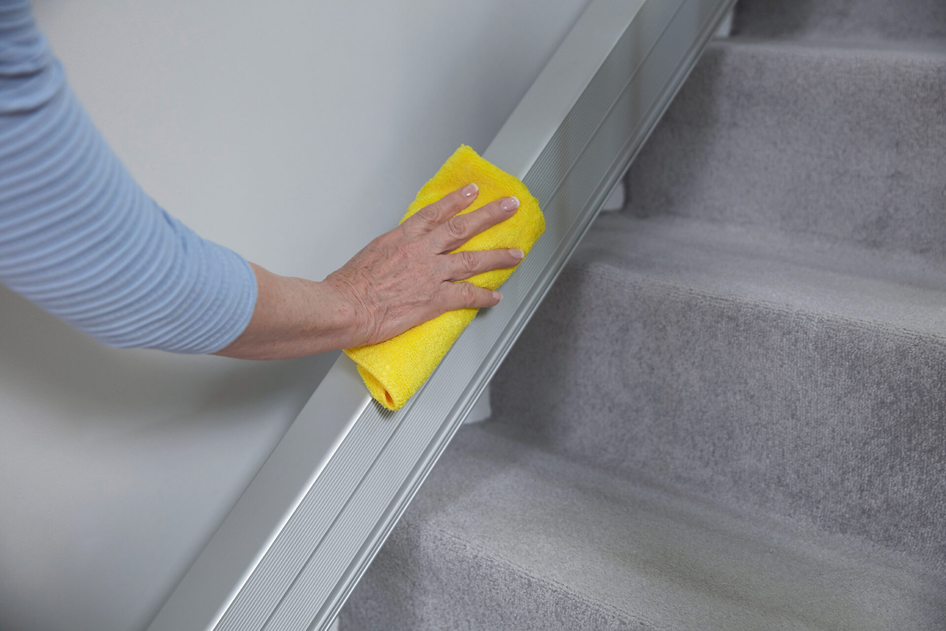 Woman cleaning the Handicare 1100 Slide Track with a yellow cloth