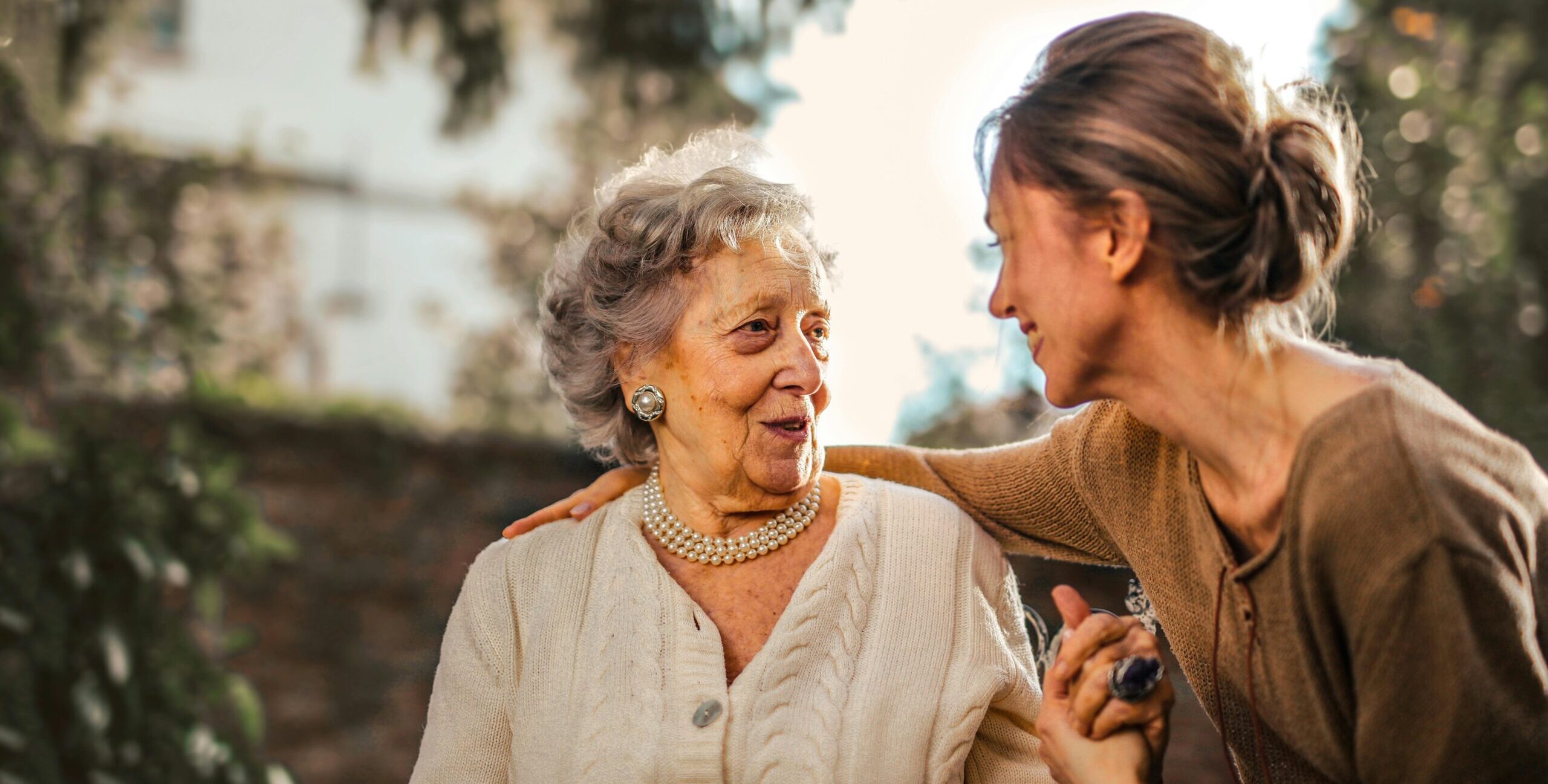 Joyful adult carer greeting happy surprised senior woman in garden