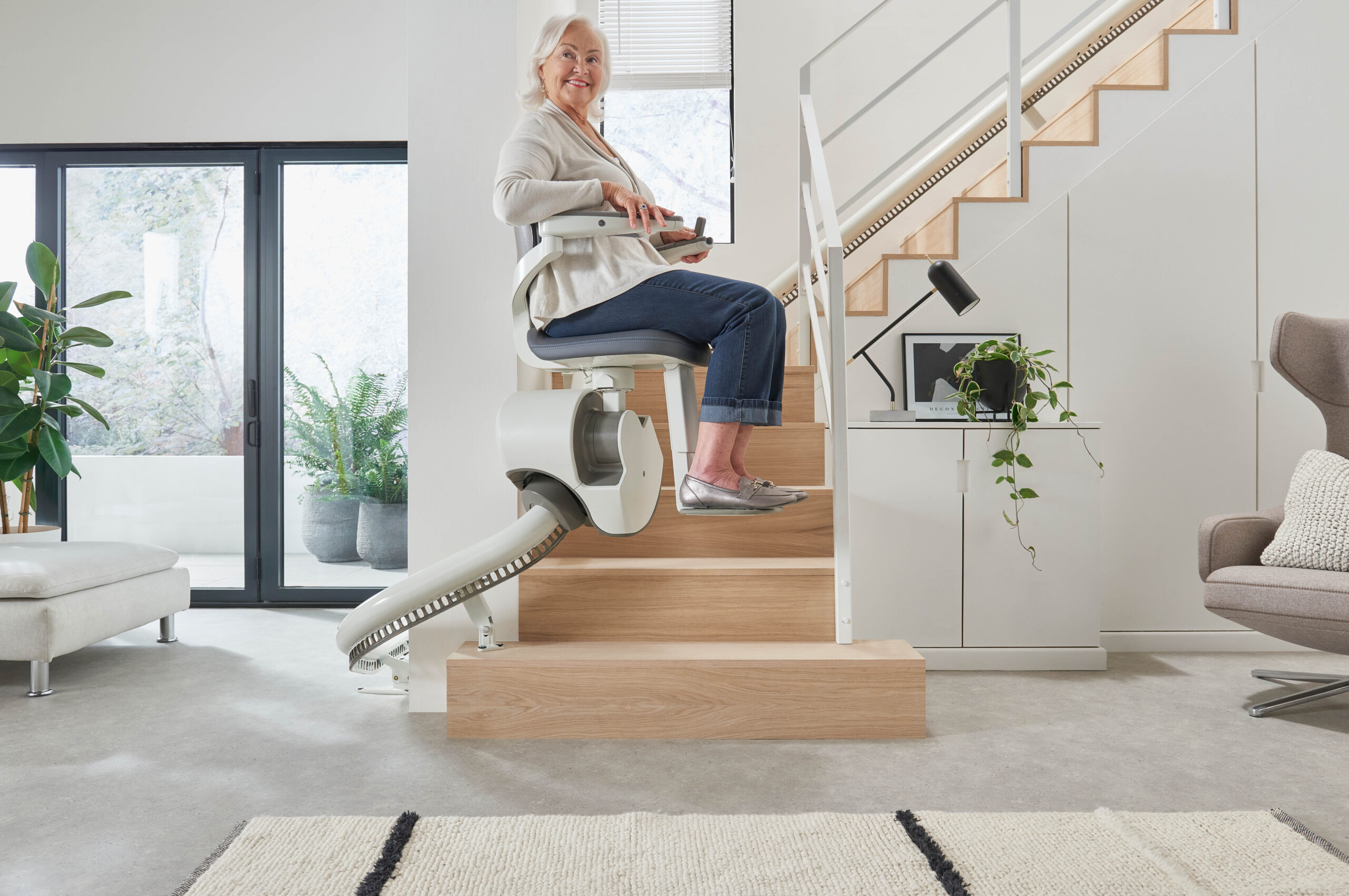 An elderly woman riding up her curved narrow stairs on a flow x stairlift