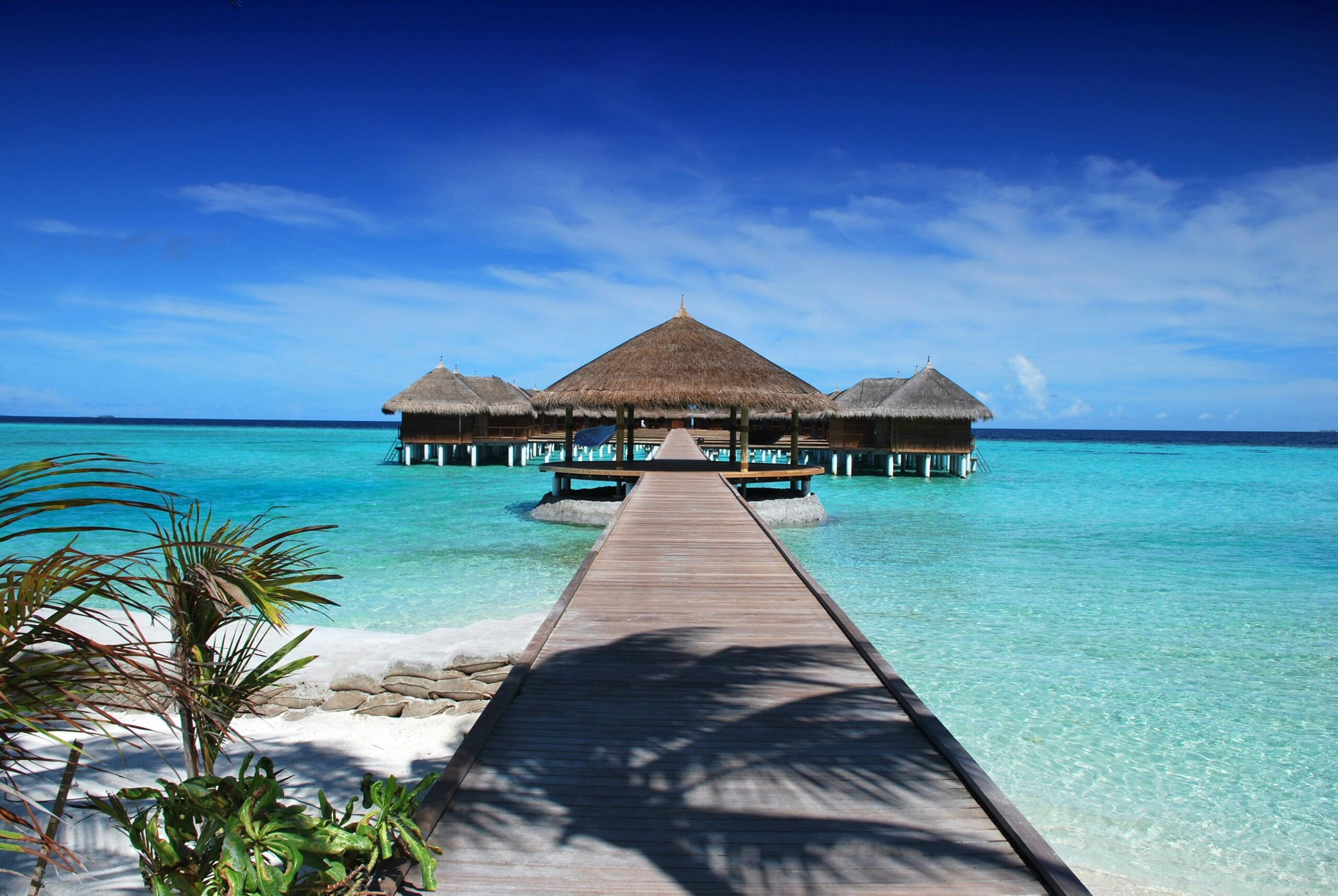 A view of a blue ocean with a sandy beach, a boardwalk & some shelter