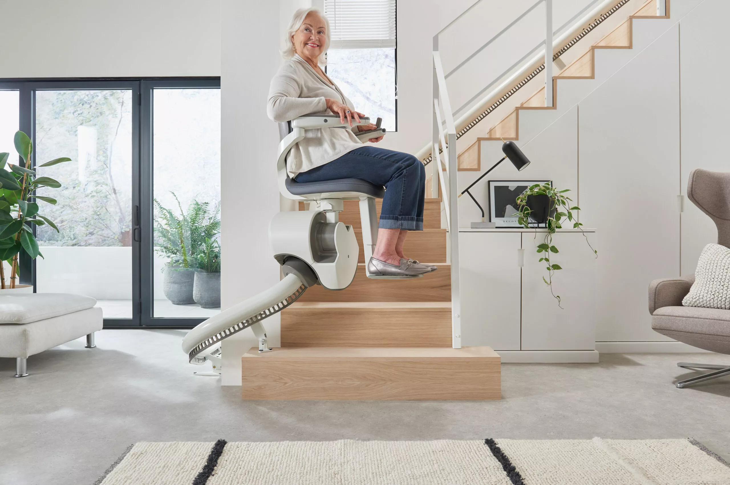 An elderly woman riding up her curved narrow stairs on a flow x stairlift