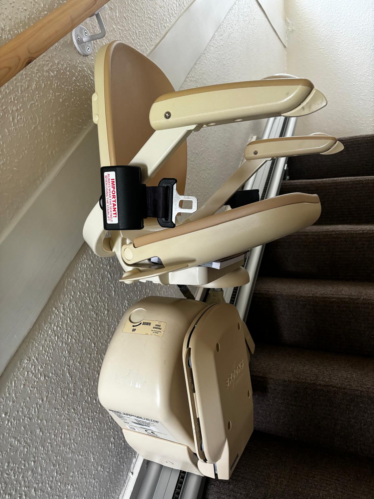 A brooks 130 straight stairlift parked comfortably at the bottom of a carpeted staircase