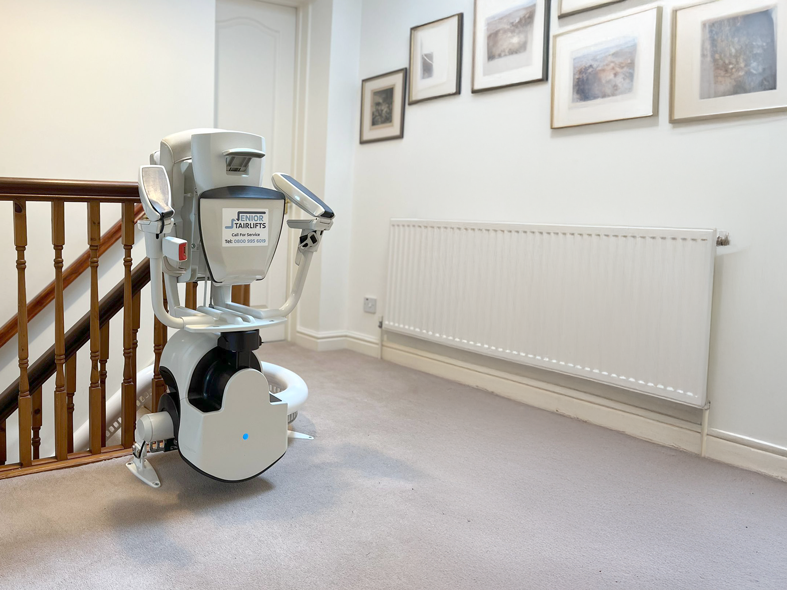 A Flow 2A Stairlift neatly parked at the top of the stairs. A Senior Stairlifts Call sticker is present on the bottom of the seat.