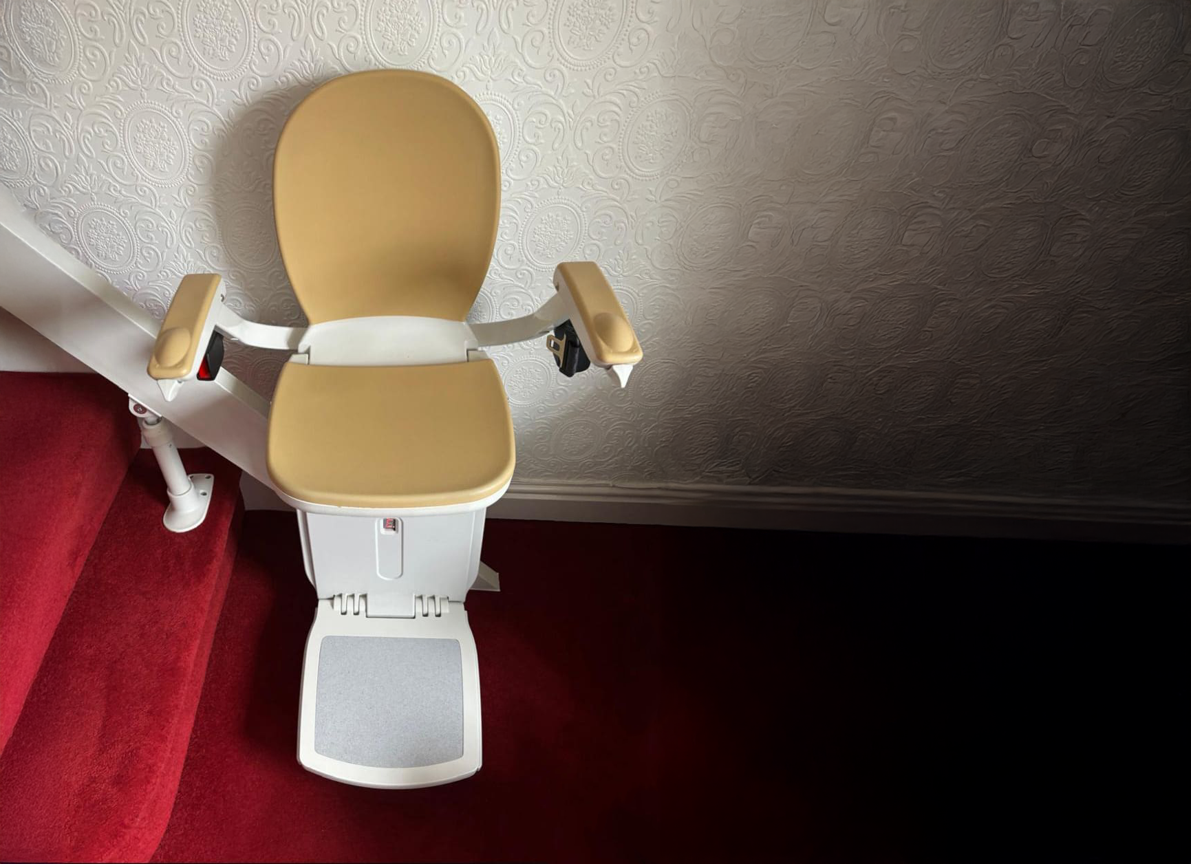 An Acorn 180 Stairlift expertly installed on a red staircase.