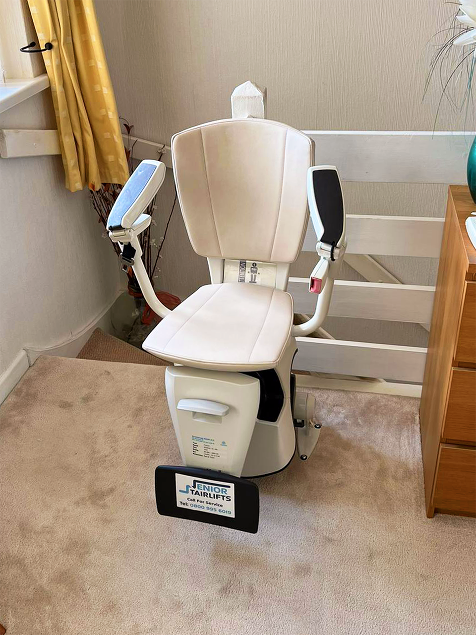 A Flow 2a stairlift with a white seat, the arms are folded up but the seat is folded down.