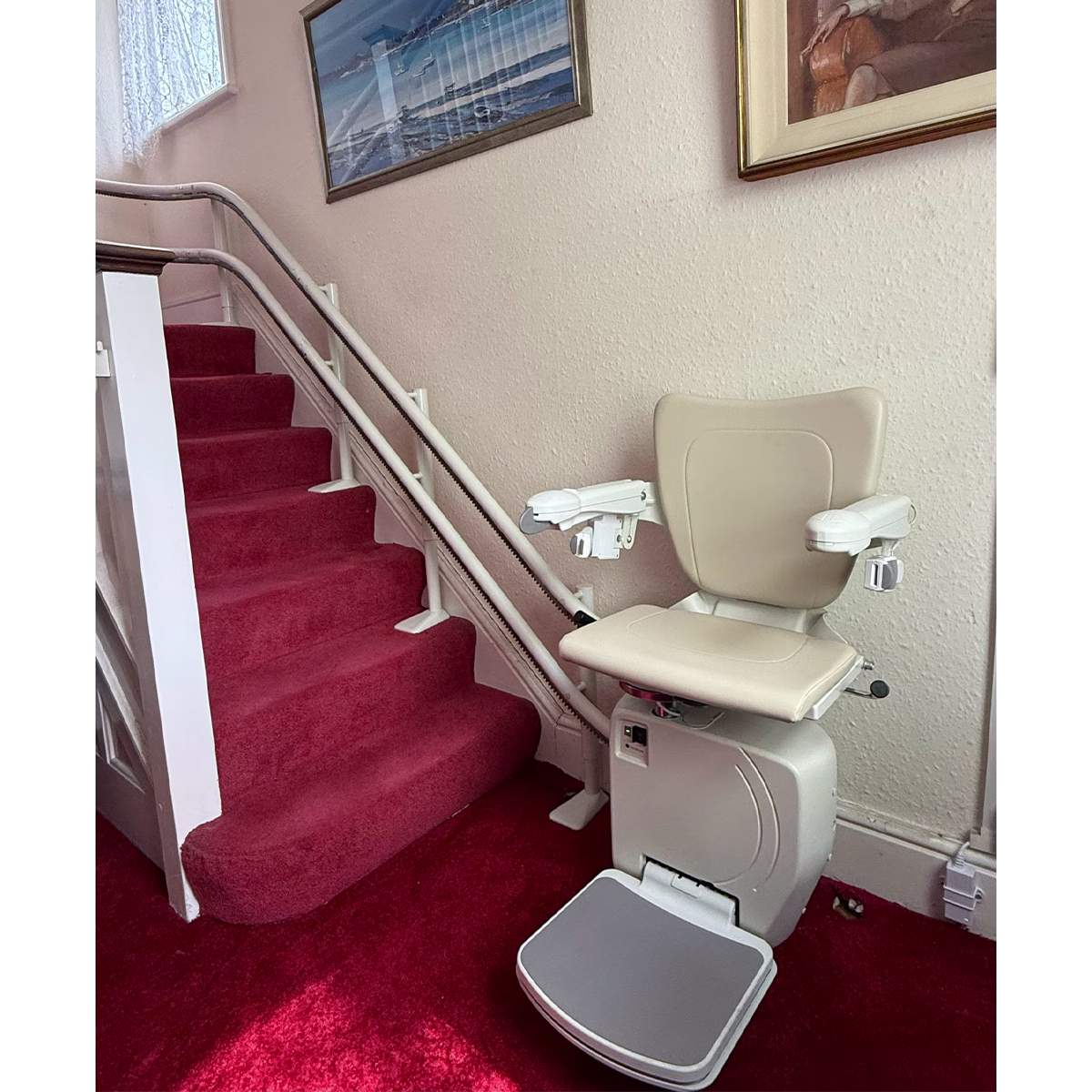 A cream coloured handicare stairlift on a red carpet