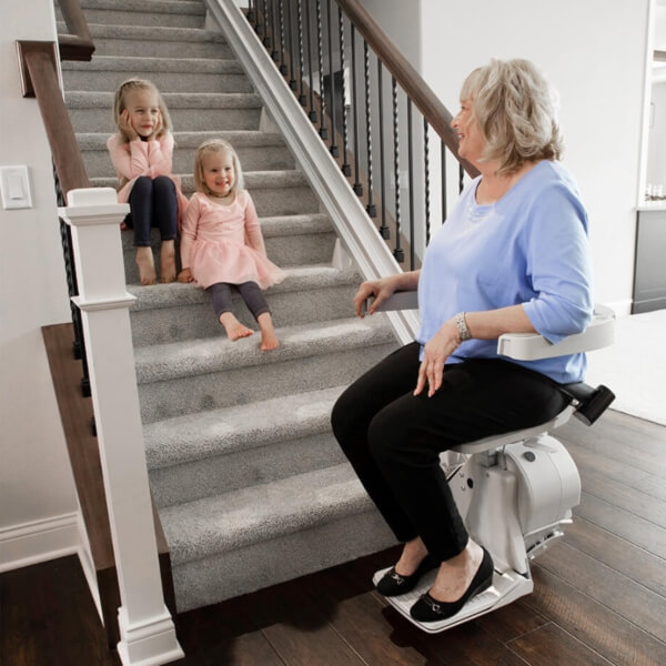 lady riding stairlift with grandkids sitting on the steps